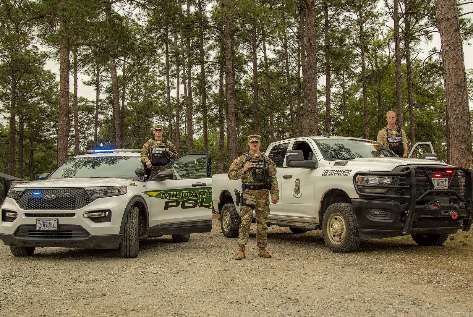 Military police personnel in outer tactical vests standing beside patrol vehicles