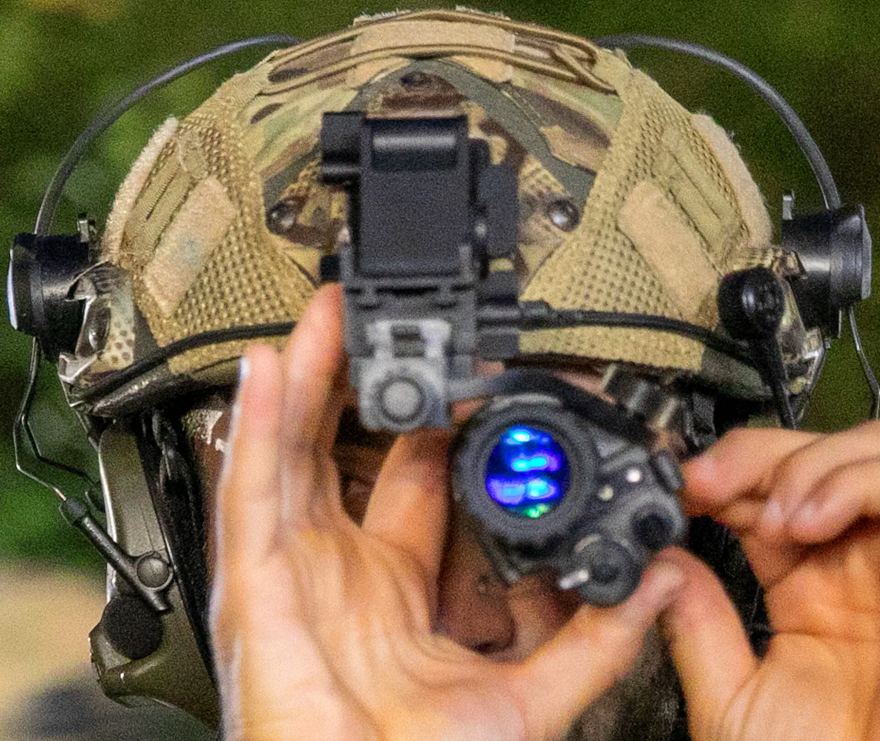 Close-up of hands adjusting a night-vision device mounted on a helmet