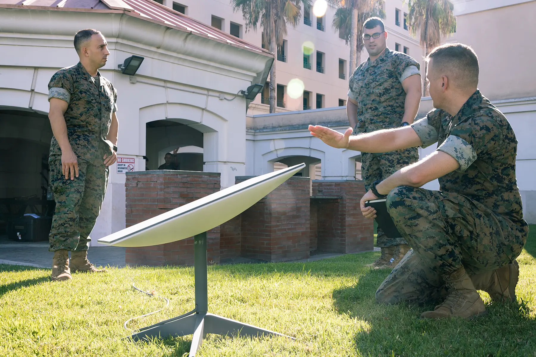 Flat-panel satellite terminal on a stand on a lawn, with personnel alongside