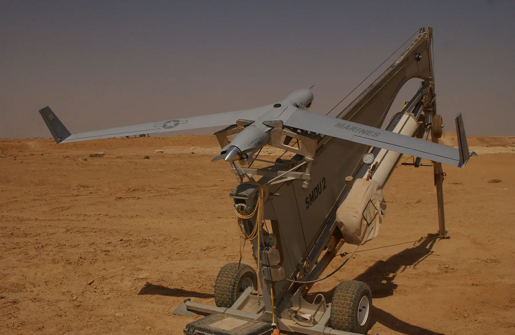 Grey fixed-wing unmanned aircraft mounted on a catapult launcher in the desert